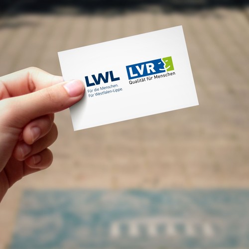 Eine Hand hält eine Visitenkarte mit den Logos vom LWL und dem LVR nebeneinander.
